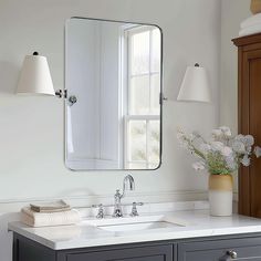 a bathroom sink with a mirror above it and flowers in a vase on the counter