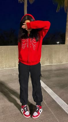 a woman in red hoodie and black pants standing next to palm trees at night