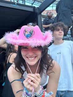 a woman wearing a pink hat with feathers on it at a music festival in front of other people