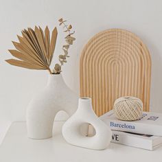 two white vases sitting on top of a table next to books and a ball of yarn