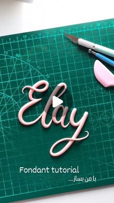 a green cutting board with scissors and some type of lettering that says, elay