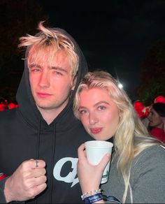 a man and woman standing next to each other holding coffee cups in front of them