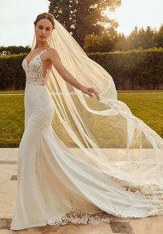 a woman in a wedding dress with a veil on her head and hands behind her back