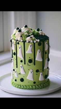 a green and white decorated cake with ghost decorations on the top, sitting on a plate in front of a window