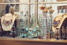 several necklaces and bracelets are on display in a window sill with glass bottles