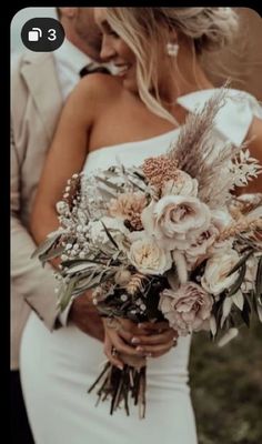 a bride and groom standing close to each other in front of the ocean holding their bouquet