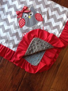 a baby blanket with an owl applique on the top and red ruffled edges