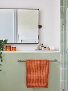 an orange towel hanging on the side of a green bathroom wall next to a mirror