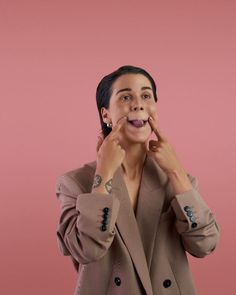 a woman is holding her hands to her face and looking at the camera while wearing a jacket