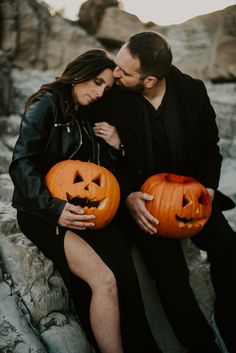 a man and woman sitting on rocks holding jack - o'- lantern pumpkins