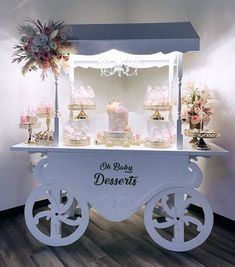 a white cart filled with lots of desserts on top of a wooden floor next to a wall