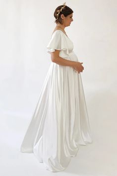 a pregnant woman in a white gown standing against a white background wearing a gold headpiece