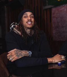 a man with dreadlocks sitting at a table in front of a wine glass