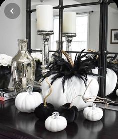 white pumpkins and black feathers sit on a dresser in front of a mirror with candles