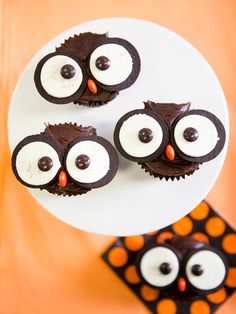 three cupcakes decorated like owls on a white plate with orange polka dot paper