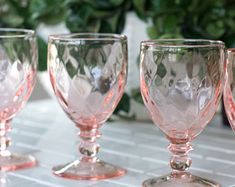 four pink glass goblets are lined up on a countertop next to a potted plant