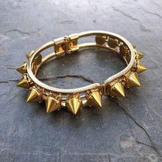 This stunning cuff is made of individually handset gold spikes in pronged settings, arranged around a hinge closure cuff. The oval shape fits comfortably on most wrists and is perfect for stacking or wearing solo. With its edgy design, this cuff will add a touch of rebellious glamour to any outfit. Whether you're dressing up for a night out or adding a little edge to your everyday look, the Helios Cuff is the perfect accessory for any occasion. DETAILS ✨𝗥𝗘𝗔𝗗𝗬 𝗧𝗢 𝗦𝗛𝗜𝗣✨ Bracelet Diamete Edgy Metal Jewelry With Spikes, Punk Style Gold Metal Bracelet, Trendy Spiked Jewelry For Parties, Gold Punk Style Metal Bracelet, Edgy Spiked Jewelry For Parties, Edgy Metal Spike Bracelets, Edgy Spiked Metal Bracelets, Gold Metal Punk Bracelets, Gold Metal Punk Bracelet