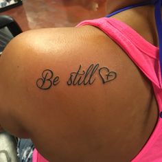 a woman's back with the words be still tattooed on her left shoulder and heart