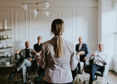 a woman standing in front of a group of people sitting down and talking to each other