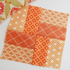 an orange and white patchwork piece on top of a table next to some fabric