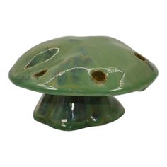 a green ceramic mushroom shaped object with holes in it's center, on a white background