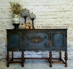 an old dresser with decorative items on top in front of a brick wall and floor