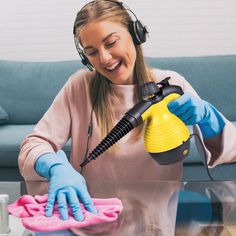 a woman wearing headphones and blue gloves is cleaning a glass table with a yellow blow dryer