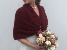 a woman wearing a red shawl holding a bouquet of white and pink flowers in her hands