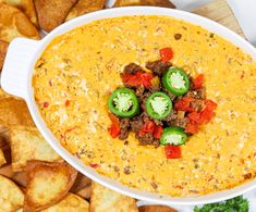 a white bowl filled with chili cheese dip surrounded by tortilla chips and jalapenos