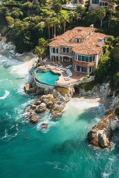 an aerial view of a large house on the shore with blue water and rocks surrounding it