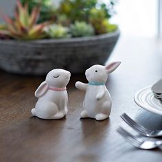 two small white rabbits sitting on top of a table next to a fork and knife