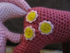 two crocheted stuffed animals are next to each other, one is pink and the other has yellow flowers