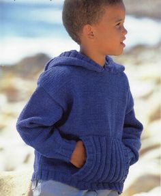 a young boy standing on top of a beach next to the ocean wearing a blue sweater