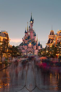 people are walking in front of the castle at disneyland's magic kingdom during twilight