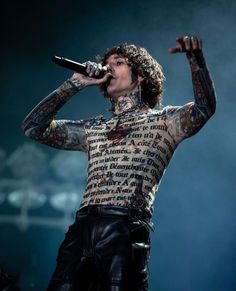 a man with tattoos and piercings on his chest holding a microphone in front of him