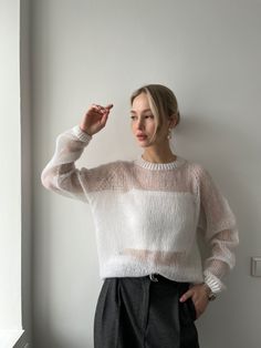 a woman standing next to a window wearing a white sweater