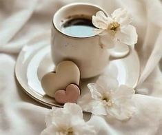 a cup of coffee and two hearts on a saucer next to some white flowers