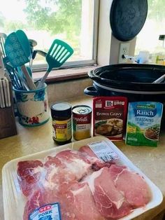 raw meat on a cutting board next to an open crock pot and other ingredients