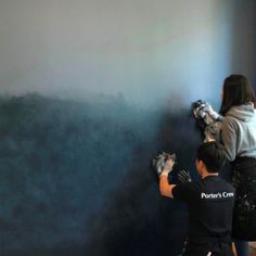 two people painting a wall with blue and gray paint on the walls, one man is holding a brush