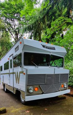 an rv parked on the side of a road in front of some trees and bushes