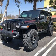 a black jeep parked in a parking lot with palm trees and buildings behind the cars