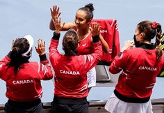 four women in red shirts and white skirts are holding their hands up to the sky