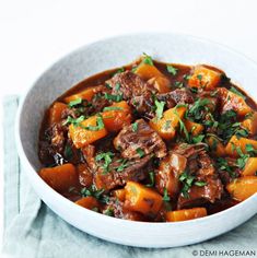 a white bowl filled with meat and carrots on top of a blue napkin next to a fork