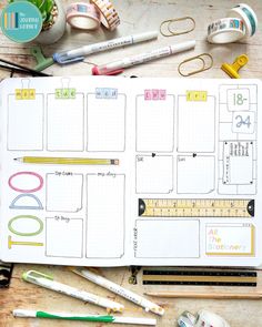 an open planner with markers, pencils and scissors on a wooden table next to other items