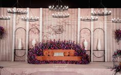 an orange couch sitting on top of a stage surrounded by purple and white floral arrangements