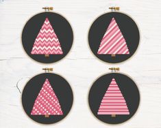 four cross stitch christmas trees in pink and white on black hoop with gold trimmings