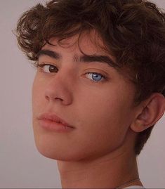 a close up of a young man with curly hair looking at the camera and to his left