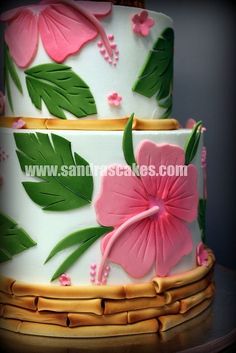 two tiered cake decorated with pink flowers and green leaves on a wooden table top