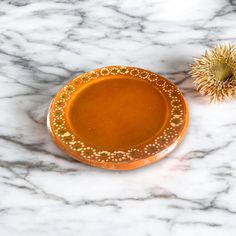 an orange bowl sitting on top of a white marble counter next to a yellow flower