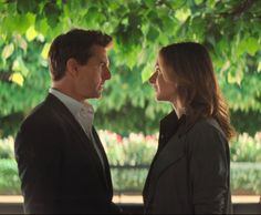 a man and woman standing next to each other in front of a tree with green leaves